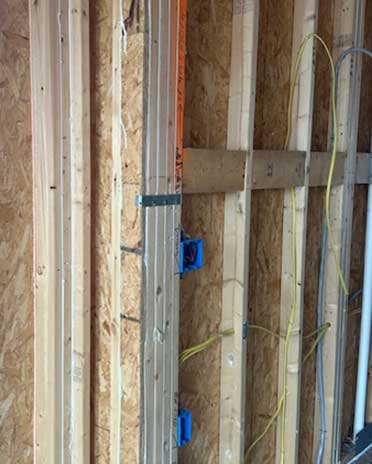 An image shows air-sealed wall joists and electrical outlets in a new construction setting, emphasizing the careful installation of insulation and sealing techniques to enhance energy efficiency and reduce air leaks