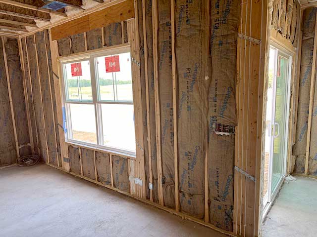 Residential fiberglass batt insulation installed in wall frame near window and sliding door.