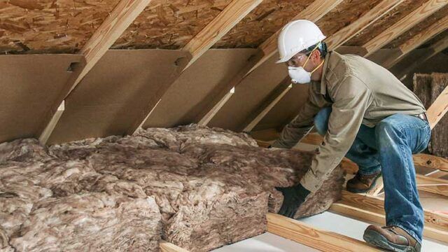 Worker installing fiberglass insulation in an attic.