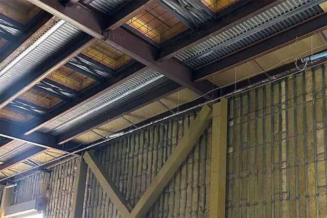 Tall industrial wall fully filled with brown mineral-wool batts behind steel framing, X-brace in foreground.