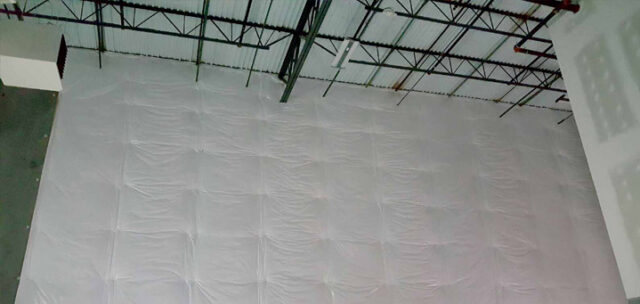 Vinyl-faced fiberglass insulation covering upper wall near roof trusses in tilt-up building.