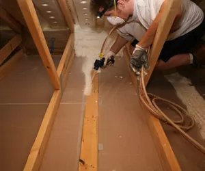 Worker air sealing the floor in an attic.