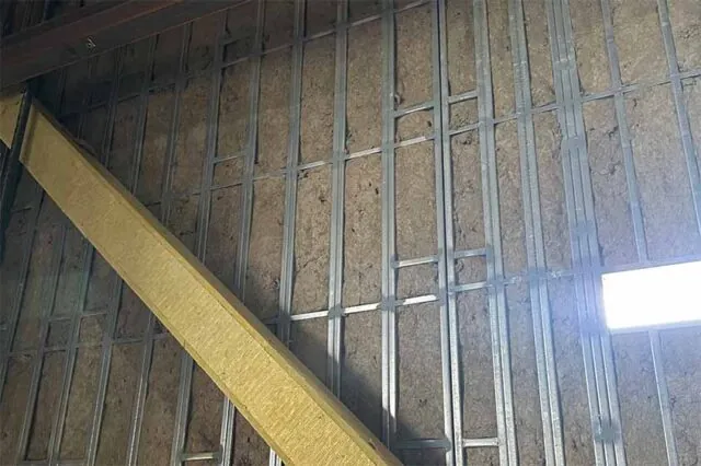 Close-up of mineral-wool batts friction-fit in a multi-story steel-furring grid.