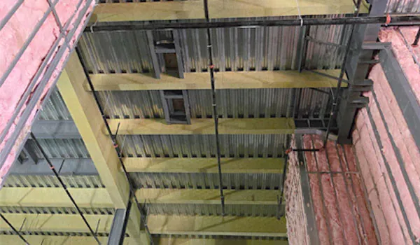 Overhead view of mineral wool fireproofing on roof beams and pink fiberglass batt insulation on walls in a data center.