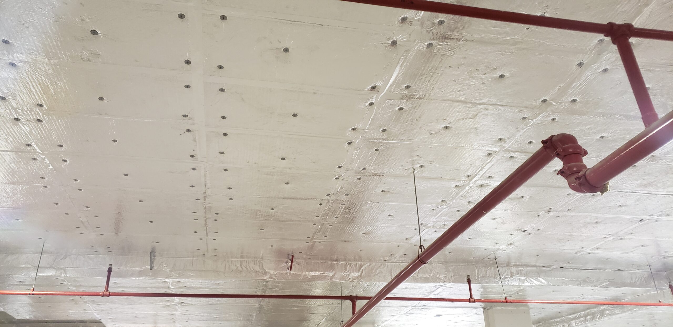 Parking garage ceiling insulated with rigid foam board.