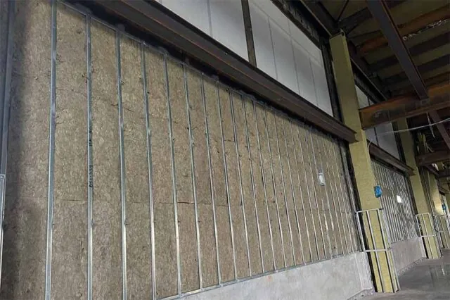 Continuous run of mineral-wool batts behind metal studs along a warehouse perimeter wall.Continuous run of mineral-wool batts behind metal studs along a warehouse perimeter wall.