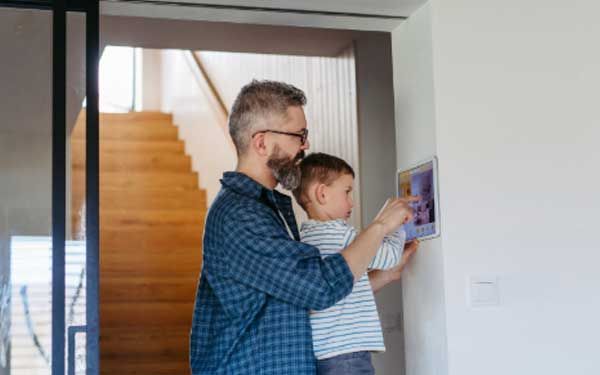 Father and son adjusting home's smart thermometer on wall.