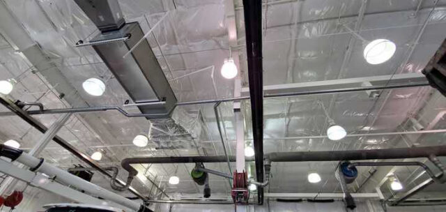 White vinyl PSK faced insulation on ceiling near piping and lighting in metal building.