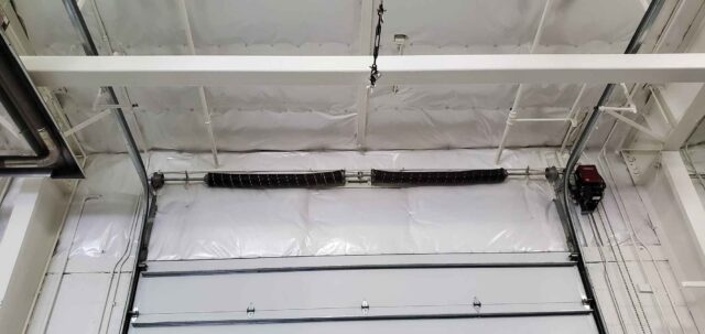 White vinyl PSK faced insulation close-up above overhead door roller in metal building.