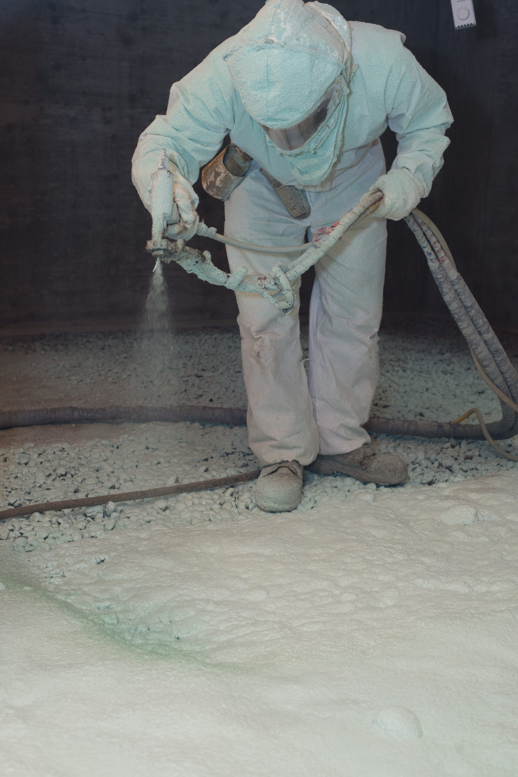 Worker in protective gear spraying insulation on a floor.